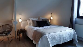A neatly made bed with a white duvet, two bedside lamps, a chair, and a nightstand.
