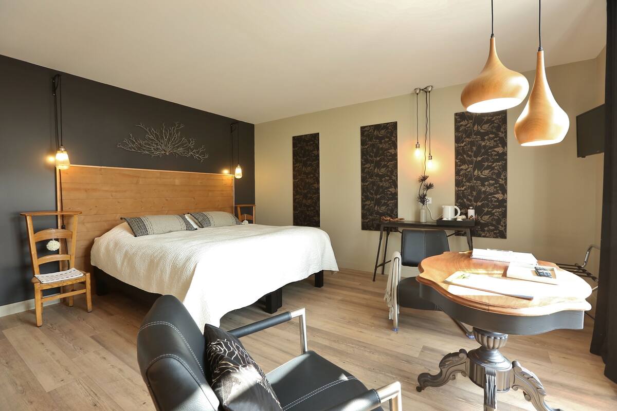 A modern bedroom with a wooden headboard, a bed with white bedding, a desk with a chair, and pendant lights.