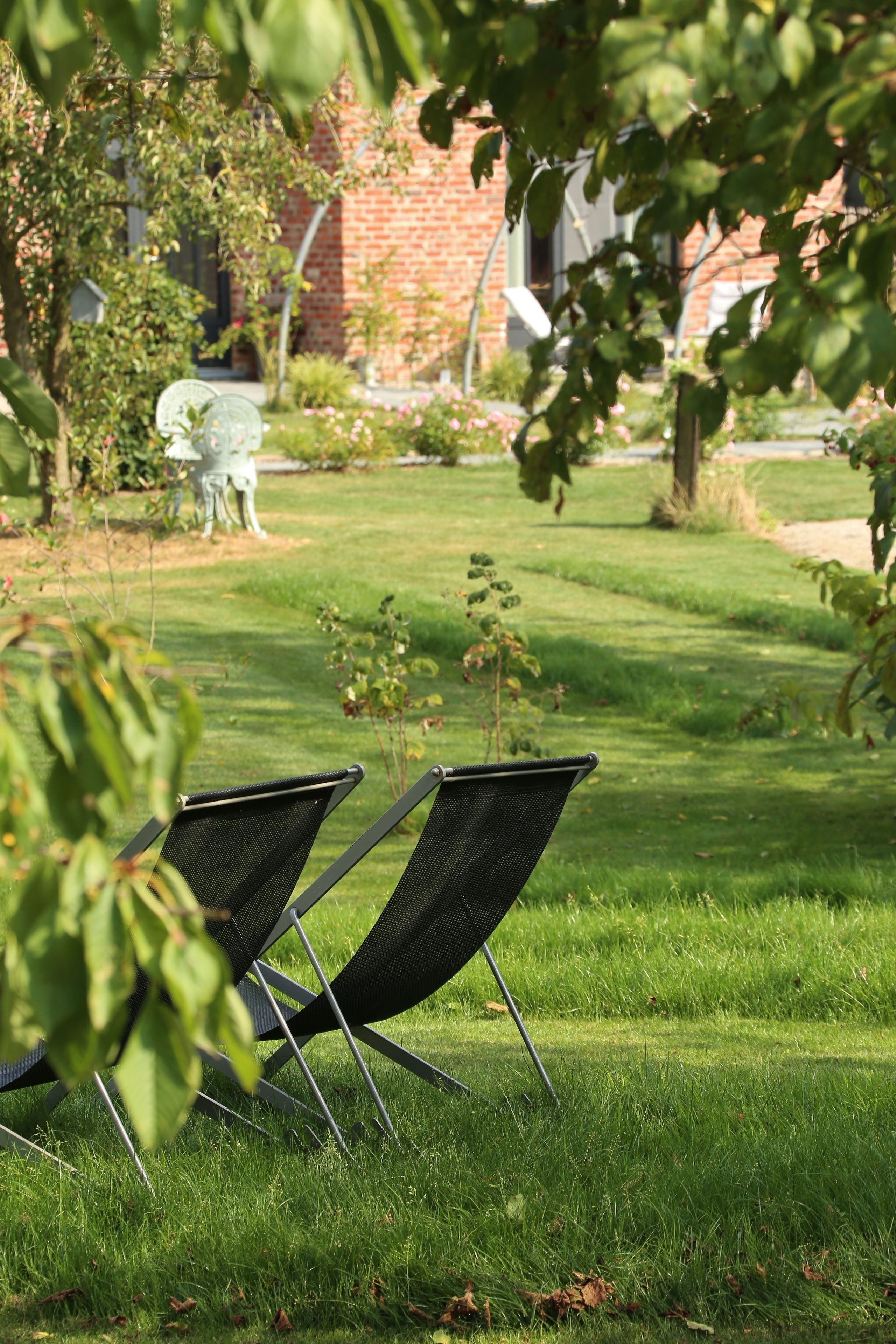 A grassy outdoor area with two black chairs and a brick building in the background.