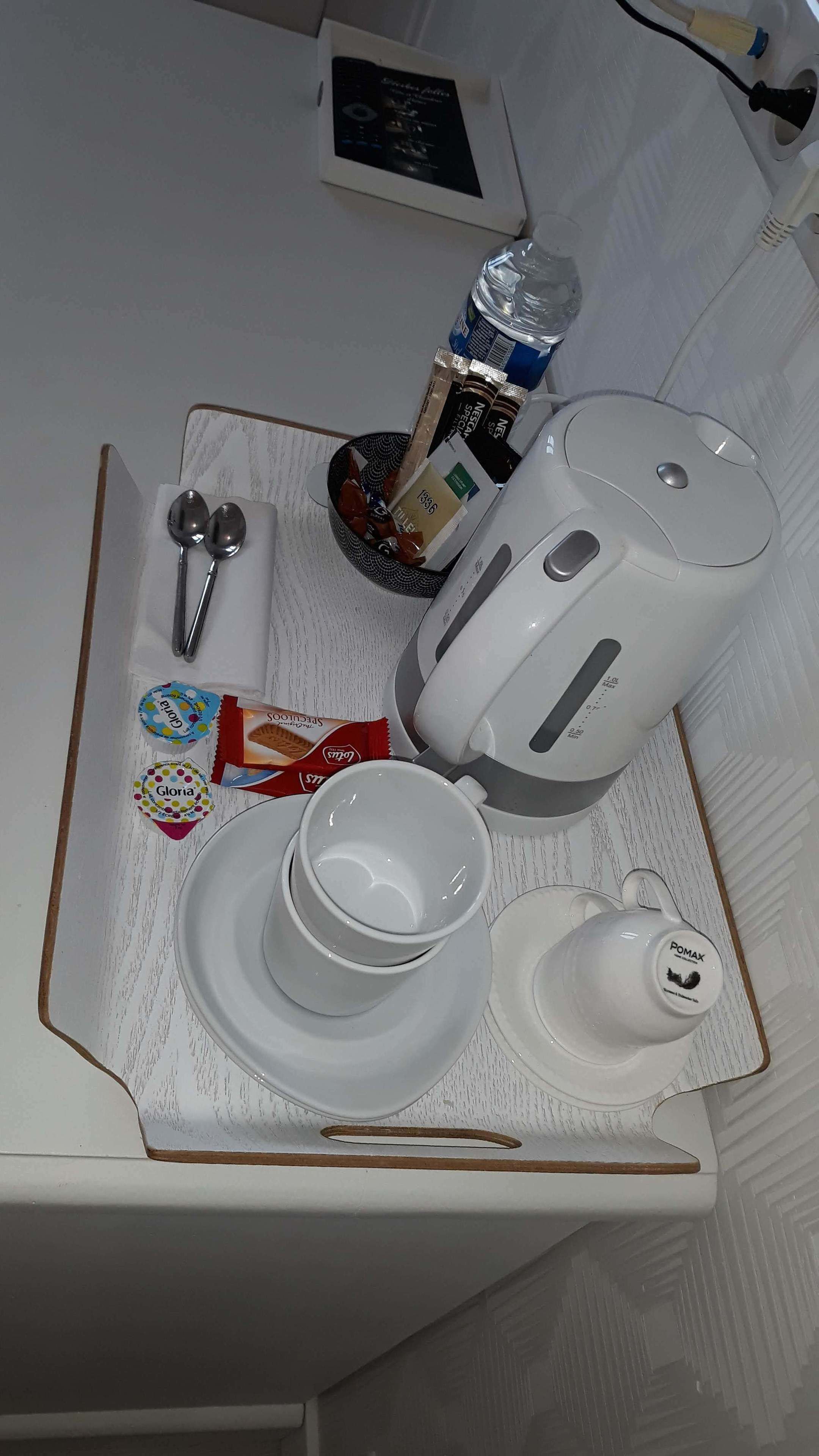 A tray with a white teapot, two cups, a spoon, a water bottle, and some packaged snacks.