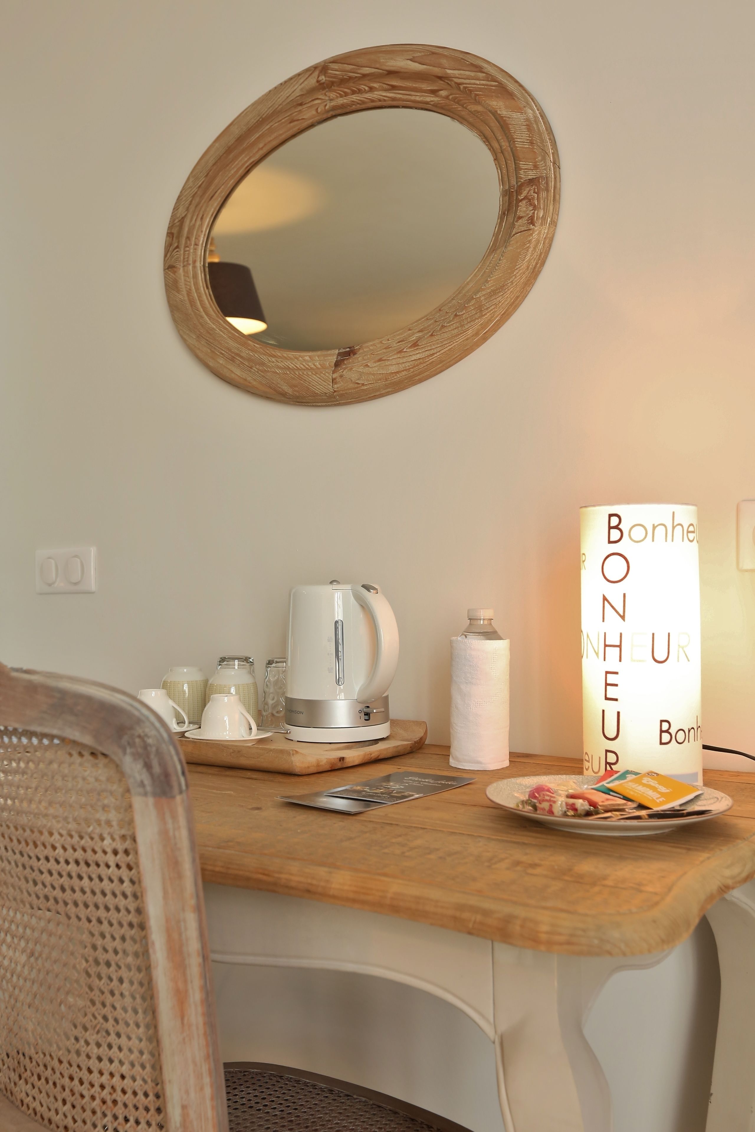 A breakfast setup with a wooden table, a kettle, a cup, a plate with food, a candle, and a mirror on the wall.