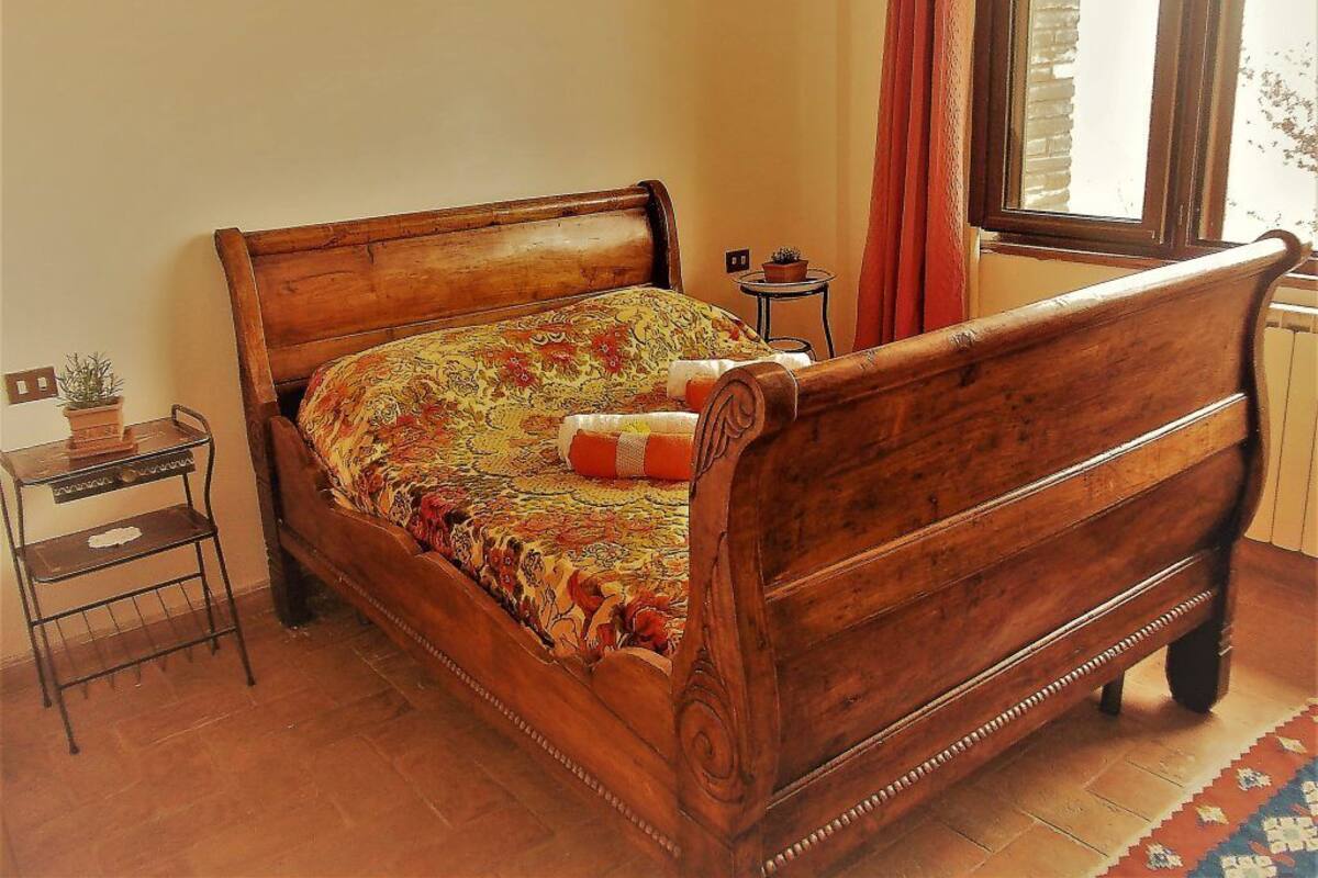 A wooden bed with a floral bedspread, a small bedside table with a lamp, and a window with curtains.