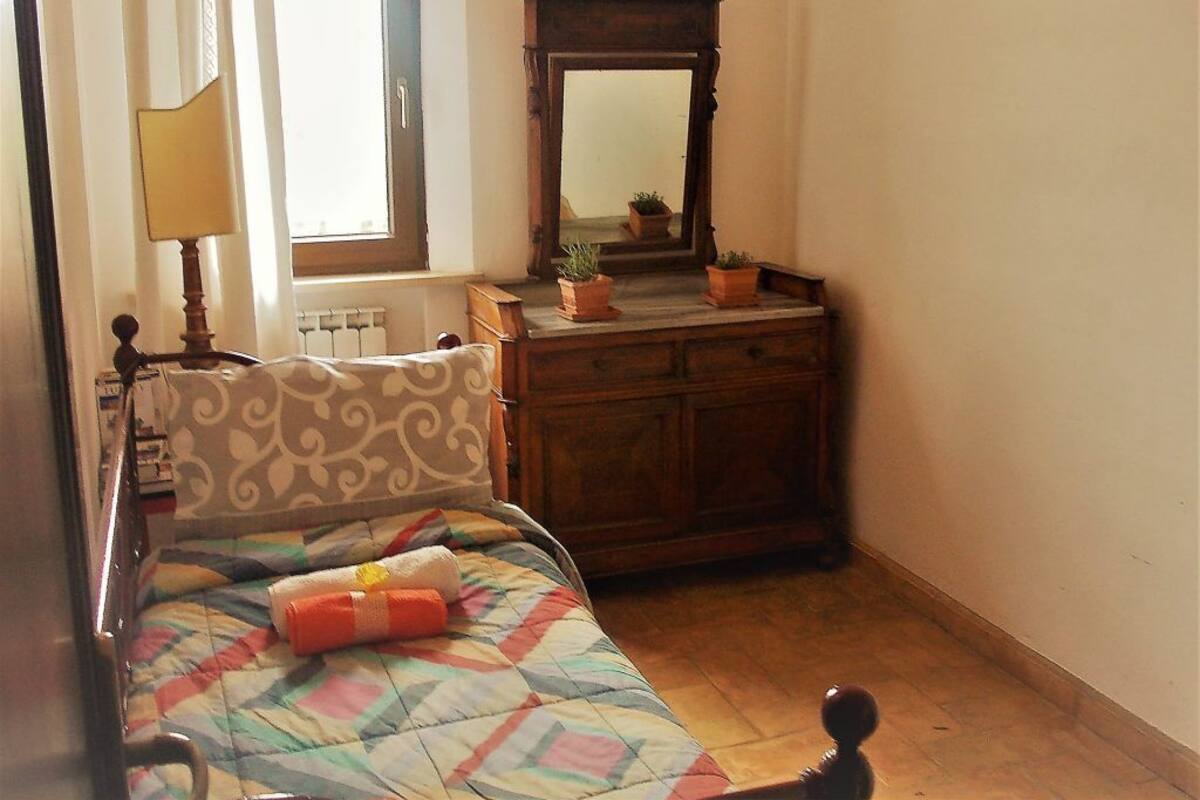 A bedroom with a bed, a dresser, a mirror, and a window with curtains.