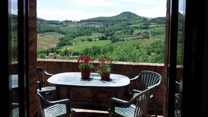 A balcony with a round table and chairs, overlooking a green landscape with hills. - Agriturismo Raggio di Sole (Montepulciano)