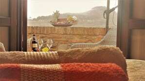 A cozy room with a view of a balcony, a wicker chair, a bottle of wine, and a bowl of fruit. - Agriturismo Raggio di Sole (Montepulciano)