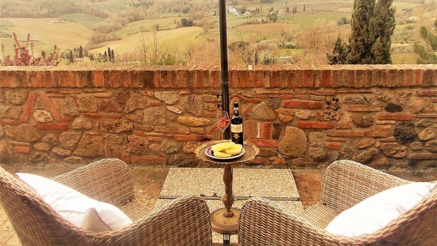 A wicker table with a bottle and glass, set against a stone wall with a view of rolling hills. - Agriturismo Raggio di Sole (Montepulciano)