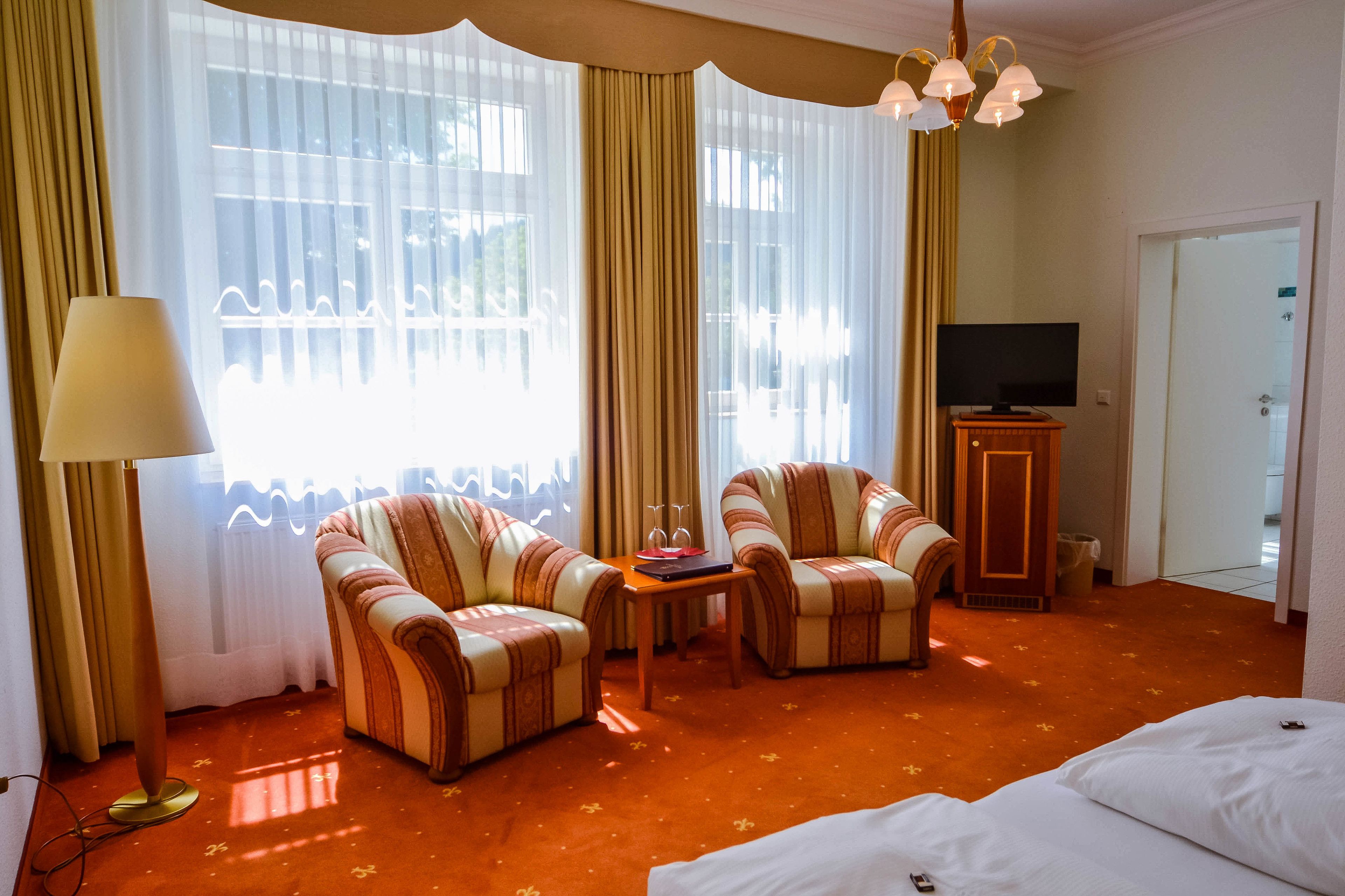 Habitación de hotel con dos sillones a rayas, una mesita con un libro y vasos, un televisor y una cama.