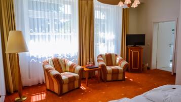 Habitación de hotel con dos sillones a rayas, una mesita con un libro y vasos, un televisor y una cama.