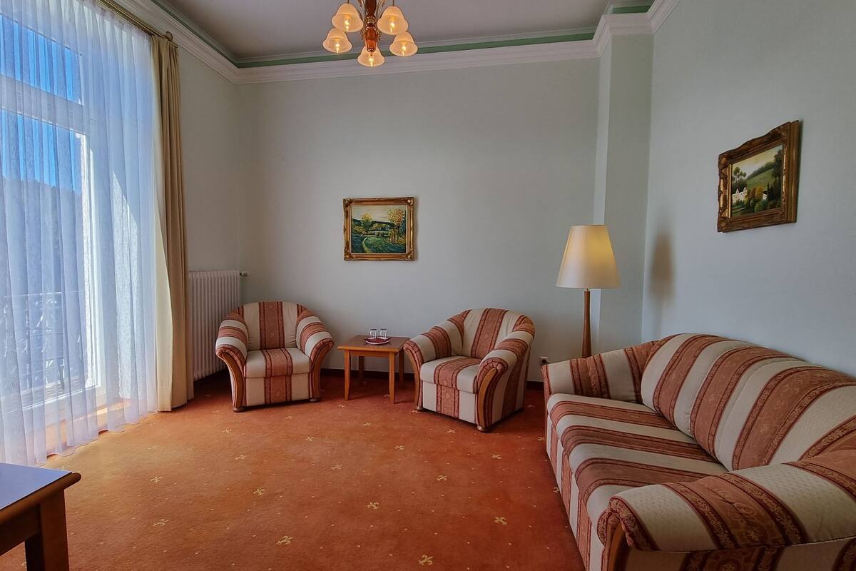 Hotelkamer met een bank, twee fauteuils, een tafeltje, een lamp en een schilderij aan de muur.