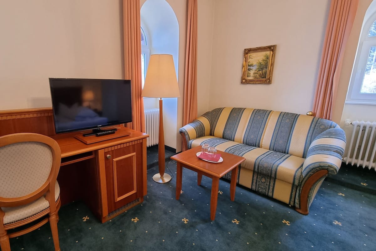 Een hotelkamer met een houten bureau, een televisie, een gestreepte bank, een klein tafeltje met glazen en een lamp.