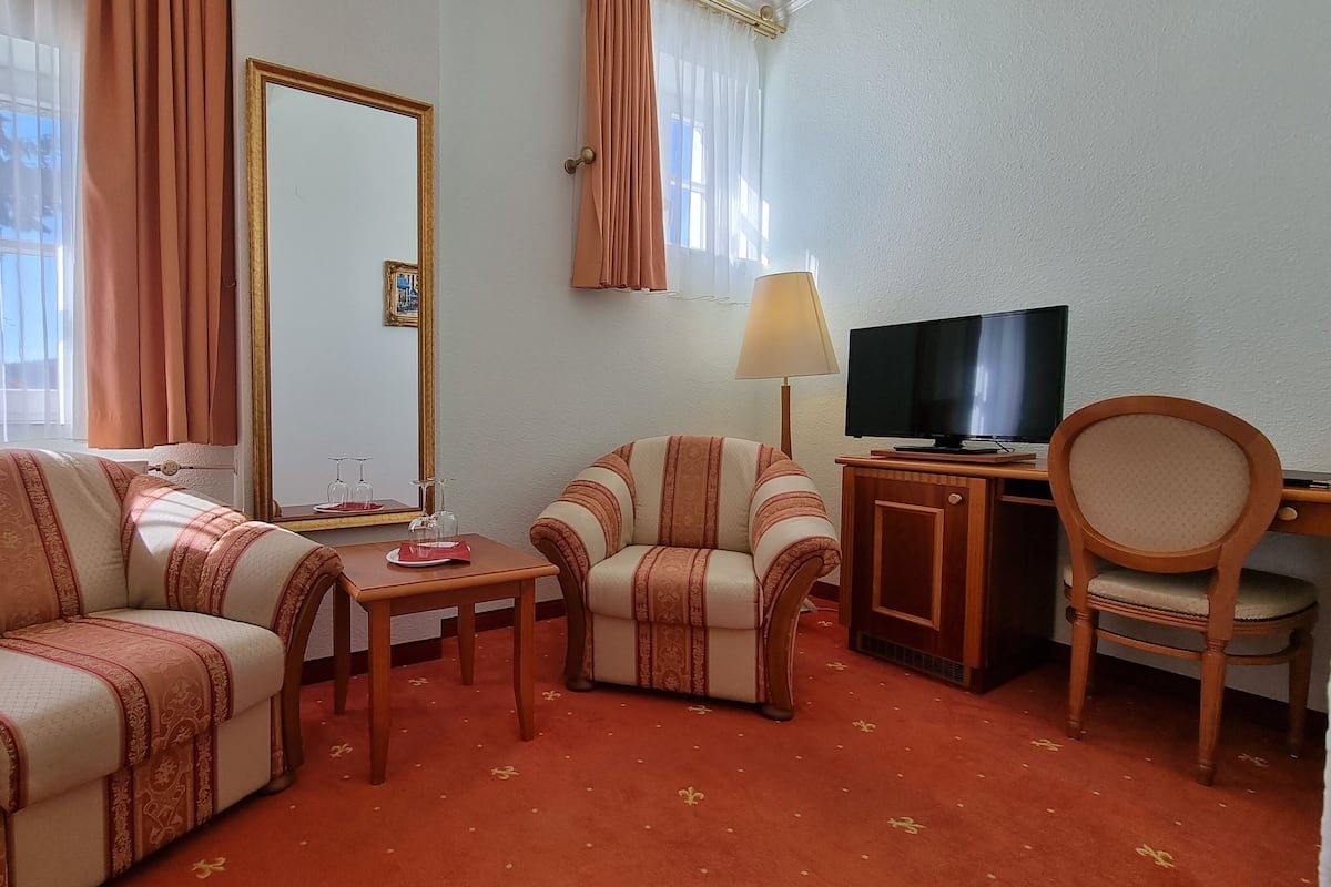 Een hotelkamer met een bank, fauteuil en een salontafel met een lamp en een televisie.
