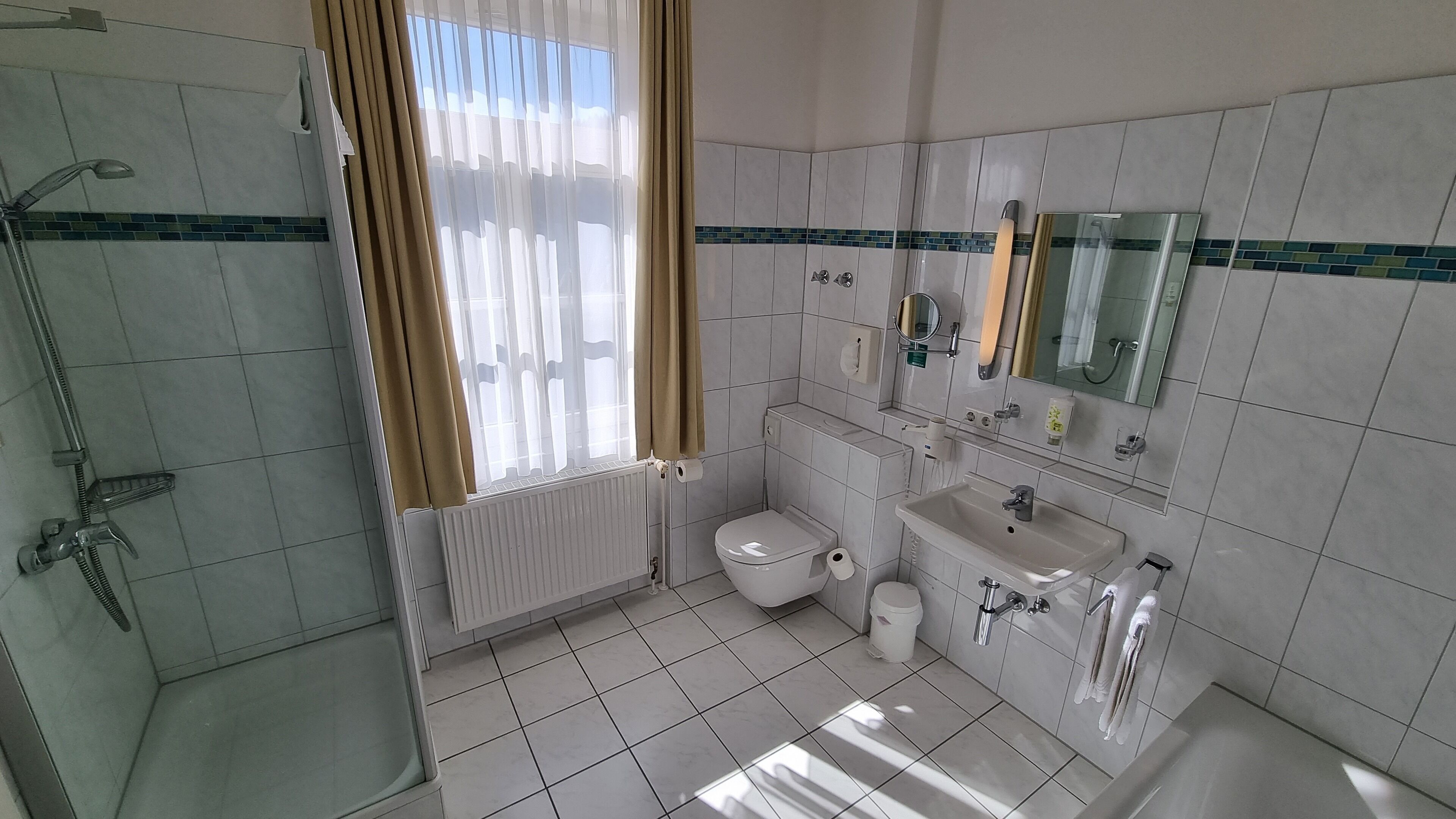 Baño con ducha, inodoro, lavamanos y espejo.