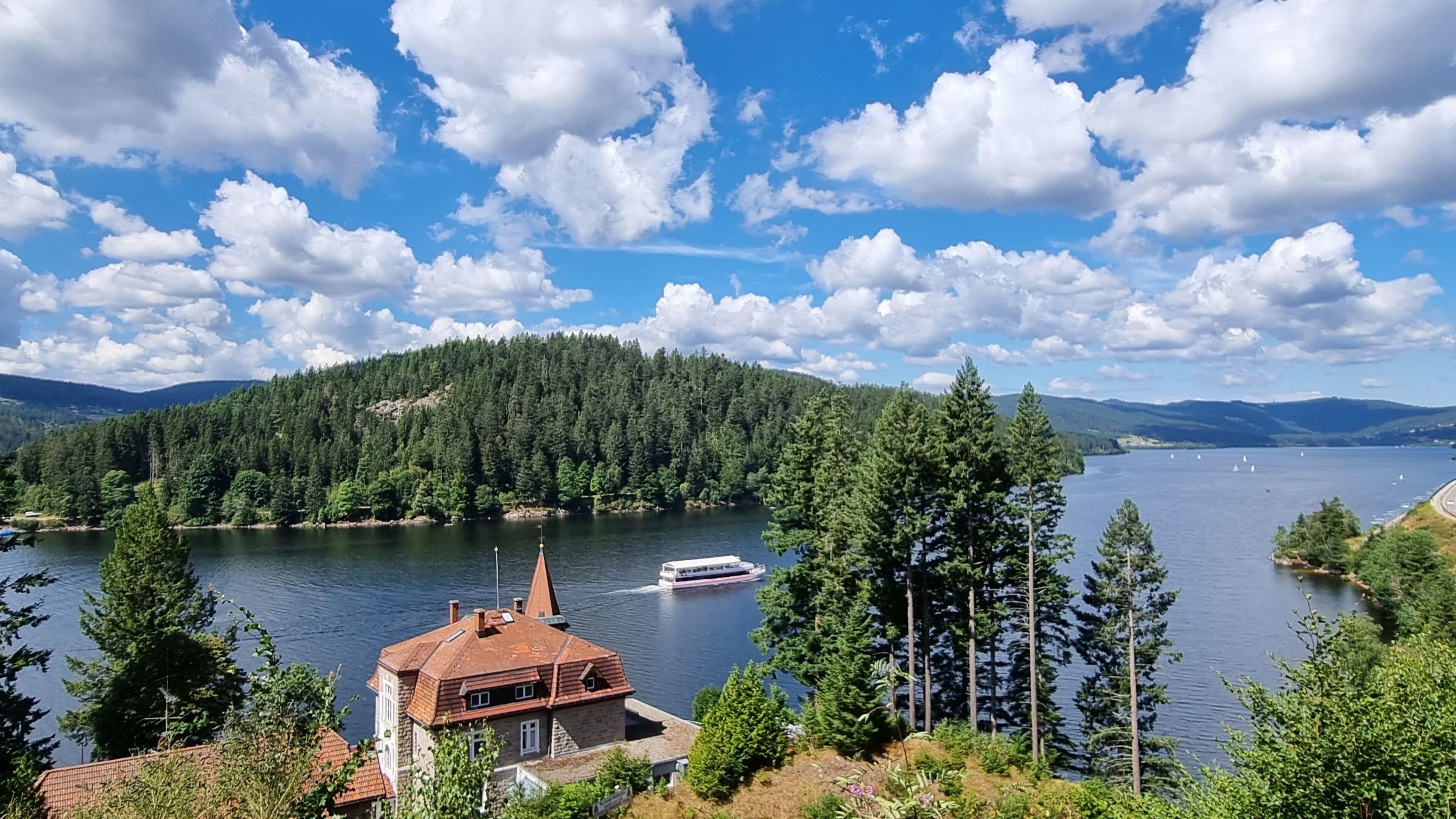A lake with a boat, surrounded by dense forest and a mountain range.