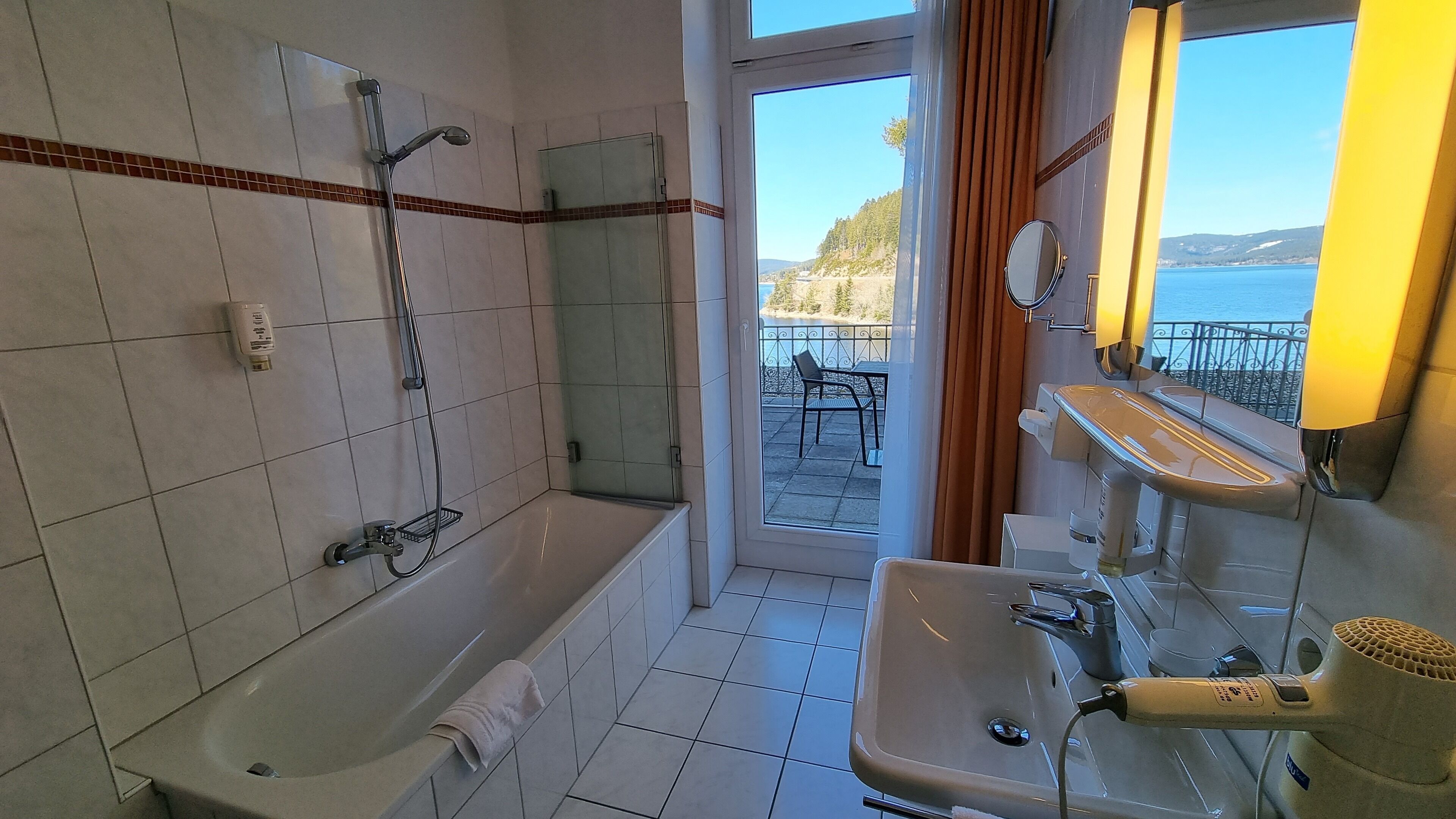 A bathroom with a bathtub, a sink, and a shower. There is a view of the outdoors through a glass door.