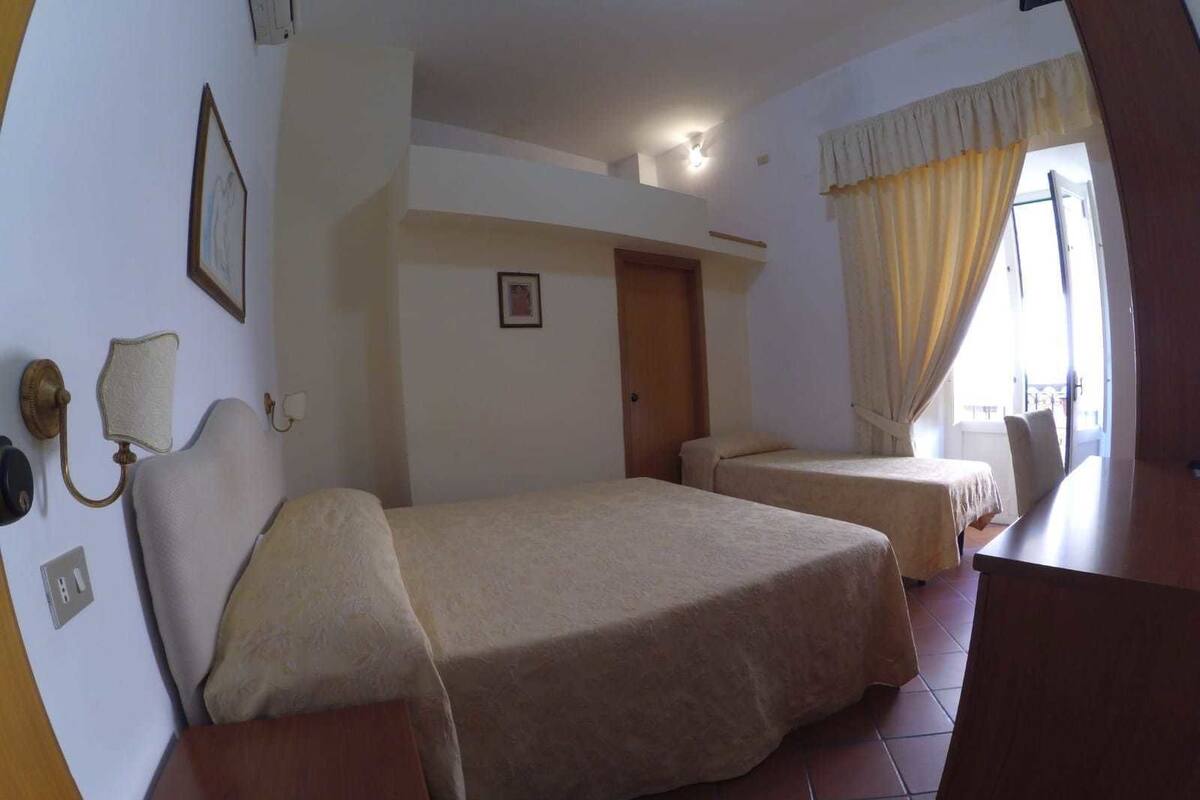Une chambre d’hôtel avec deux lits, un bureau en bois, une lampe fixée au mur et une fenêtre avec des rideaux.