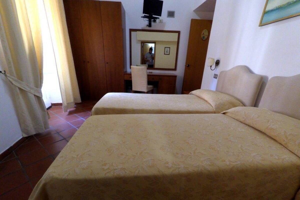 Une chambre d’hôtel avec deux lits, un bureau, une chaise, une télévision et un miroir.