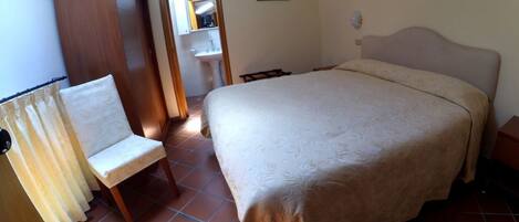 A bedroom with a bed, a chair, a wardrobe, and a bathroom visible through an open door.