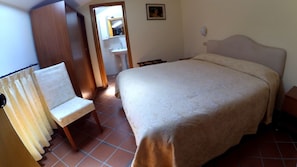 A bedroom with a bed, a chair, a wardrobe, and a bathroom visible through an open door. - Caterina House (San Lucido)