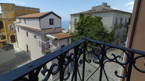 A balcony with wrought iron railings overlooking a cityscape with historic buildings and a view of the sea. - Caterina House (San Lucido)