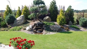 A landscaped garden with a small water feature, large rocks, and various shrubs. - Willa Pod Cyprysami (Ustka)