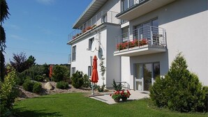 A modern two-story building with balconies, a well-maintained garden, and outdoor seating. - Willa Pod Cyprysami (Ustka)