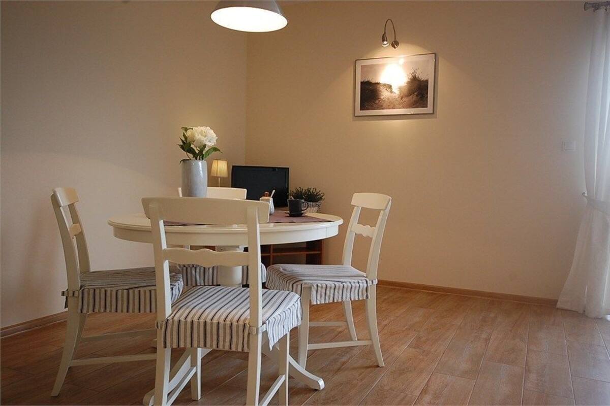 A dining area with a round table, four striped chairs, a vase with flowers, a laptop, and a framed picture on the wall.