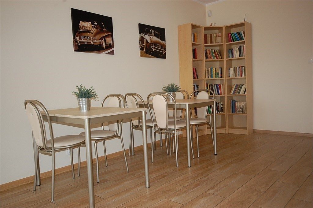 A dining area with a table and chairs, a bookshelf, and two wall-mounted pictures.
