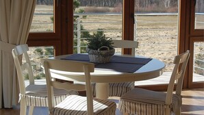 A round table with four striped chairs, a woven basket with a plant, and a view of a field through large windows. - Willa Pod Cyprysami (Ustka)