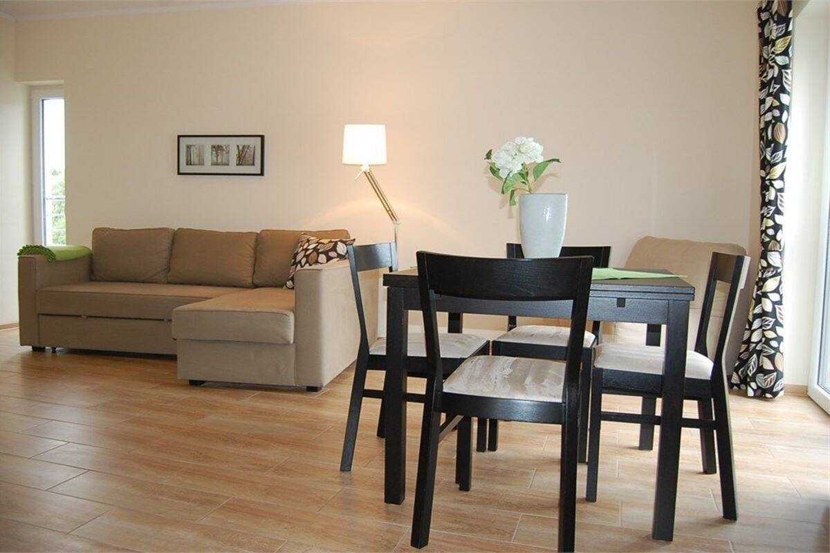 A living room with a sofa, a dining table with chairs, a lamp, and a vase with flowers.