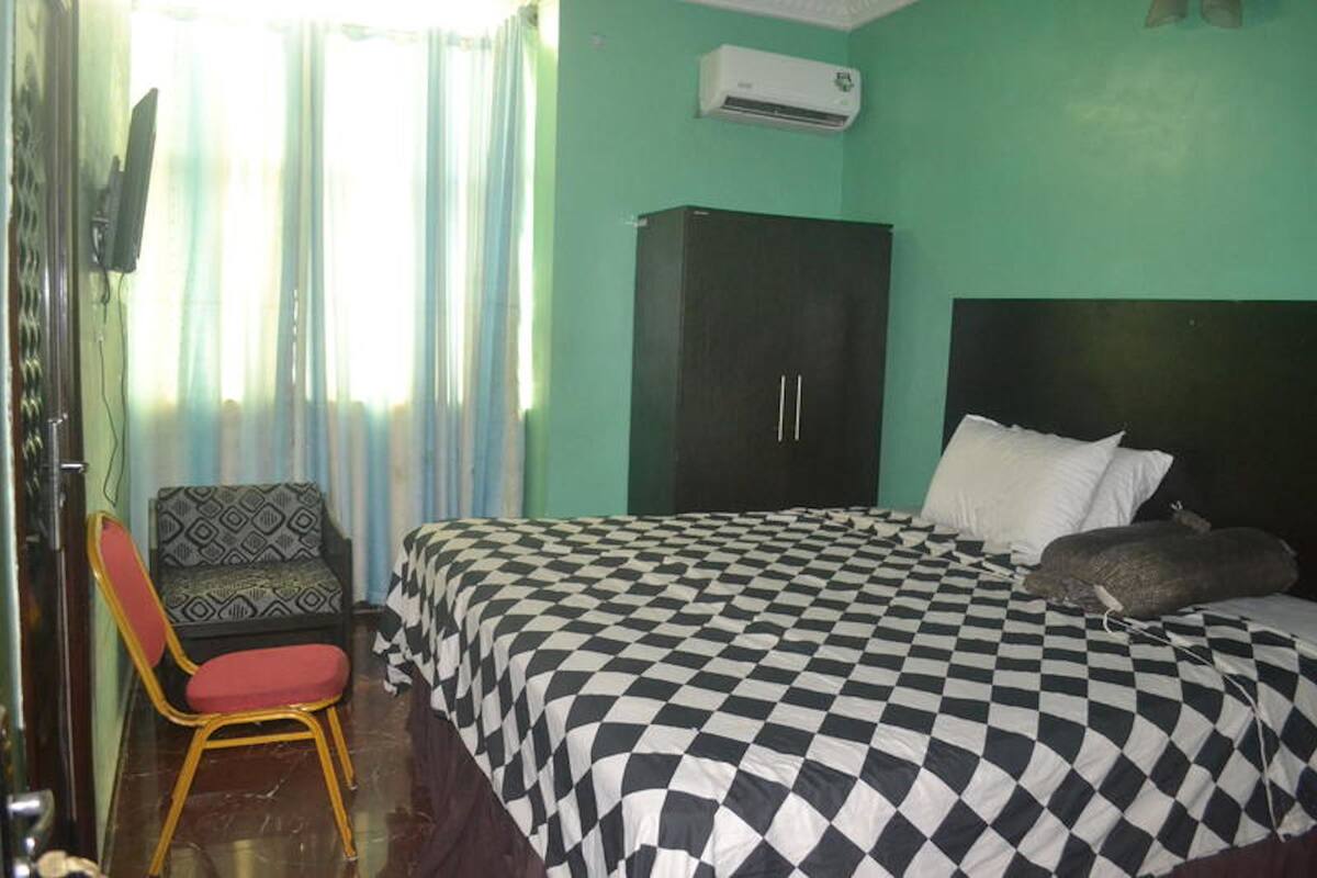 A room with a bed, a chair, a wardrobe, and an air conditioning unit.