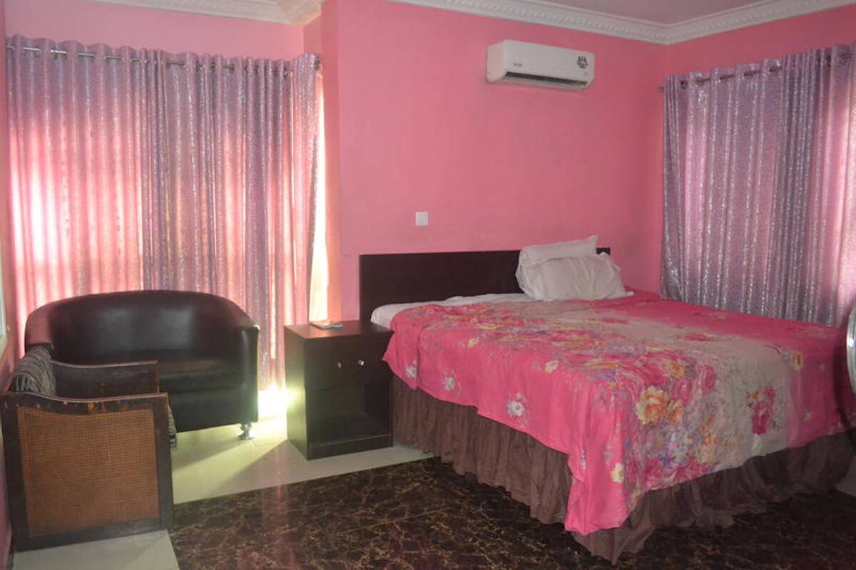 A bedroom with a bed, a nightstand, a chair, and a sofa.