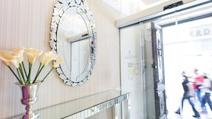 Un espace d’accueil avec un miroir, un vase de fleurs et une porte vitrée donnant sur la rue.
