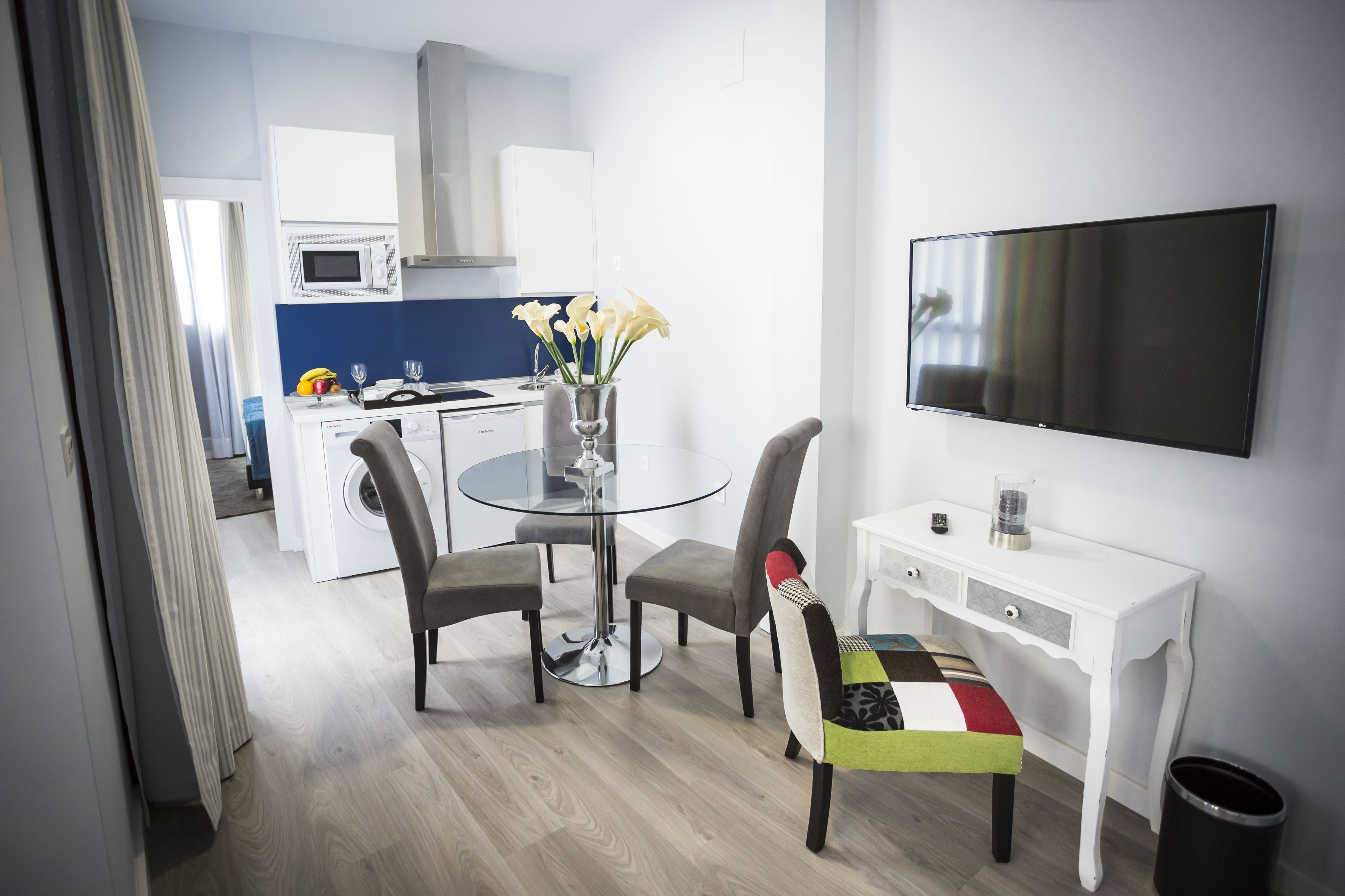 Una cocina moderna con microondas, estufa y lavaplatos. Hay una mesa de comedor con sillas y un televisor en la pared.