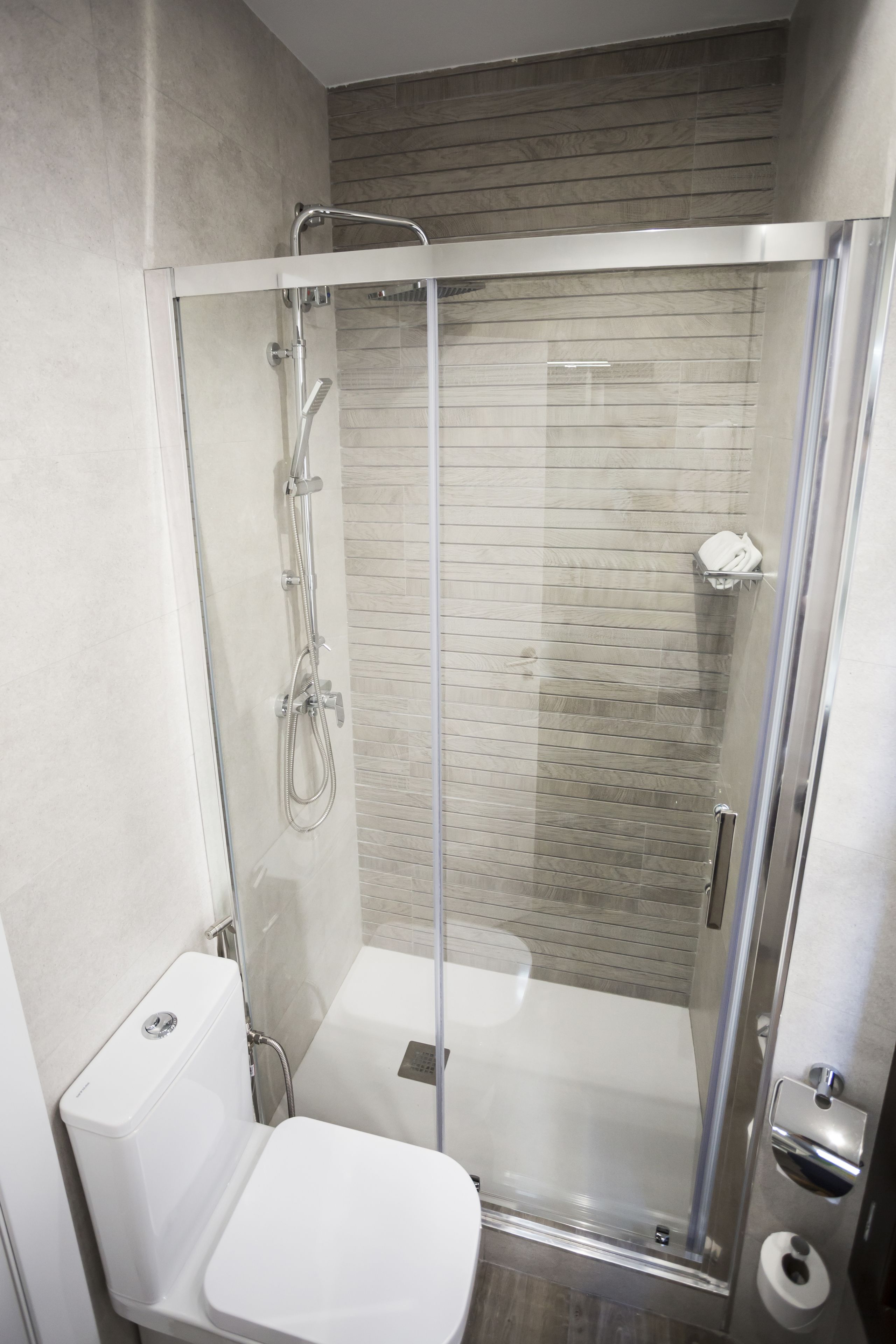 Ein modernes Badezimmer mit einer Duschkabine aus Glas, einer weißen Toilette und einer gefliesten Rückwand.