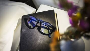 A pair of glasses on a black box, a white pillow, and a vase with flowers.