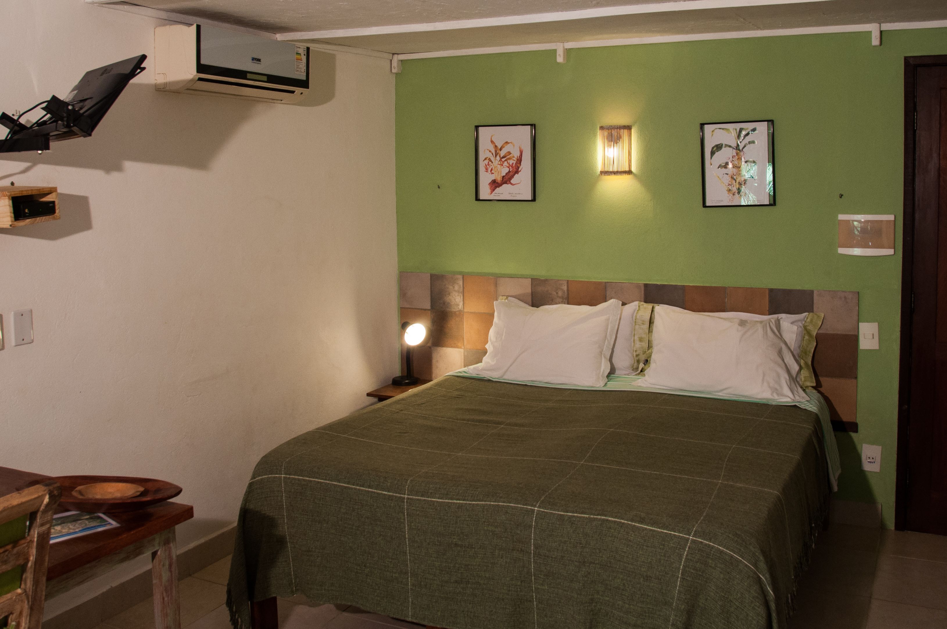 Una habitación con una cama, una mesita de noche con lámpara y dos cuadros enmarcados en la pared.