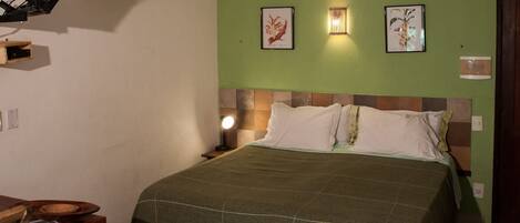 Una habitación con una cama, una mesita de noche con lámpara y dos cuadros enmarcados en la pared.