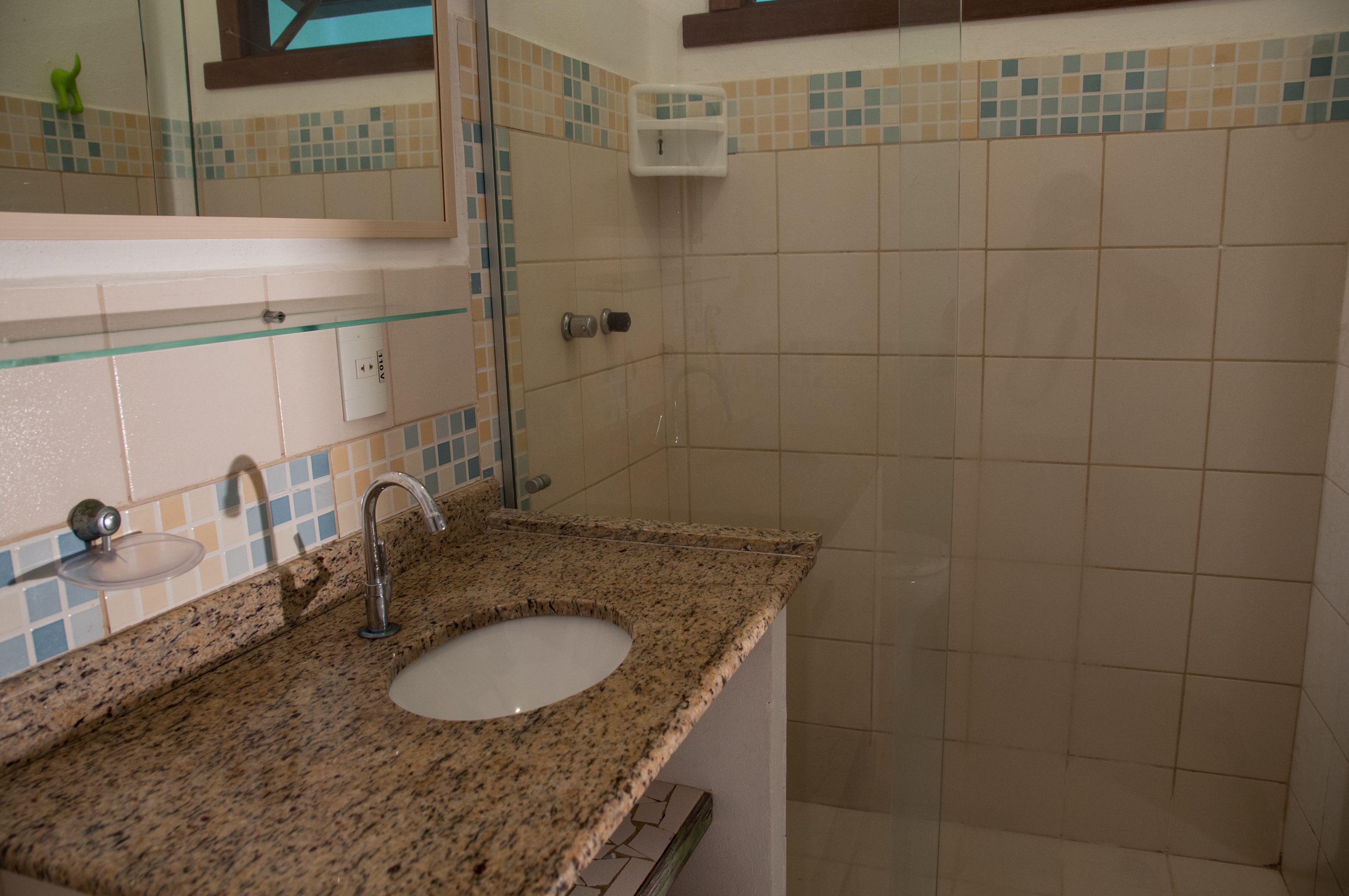 A bathroom with a granite countertop sink, a mirror, and a shower area.