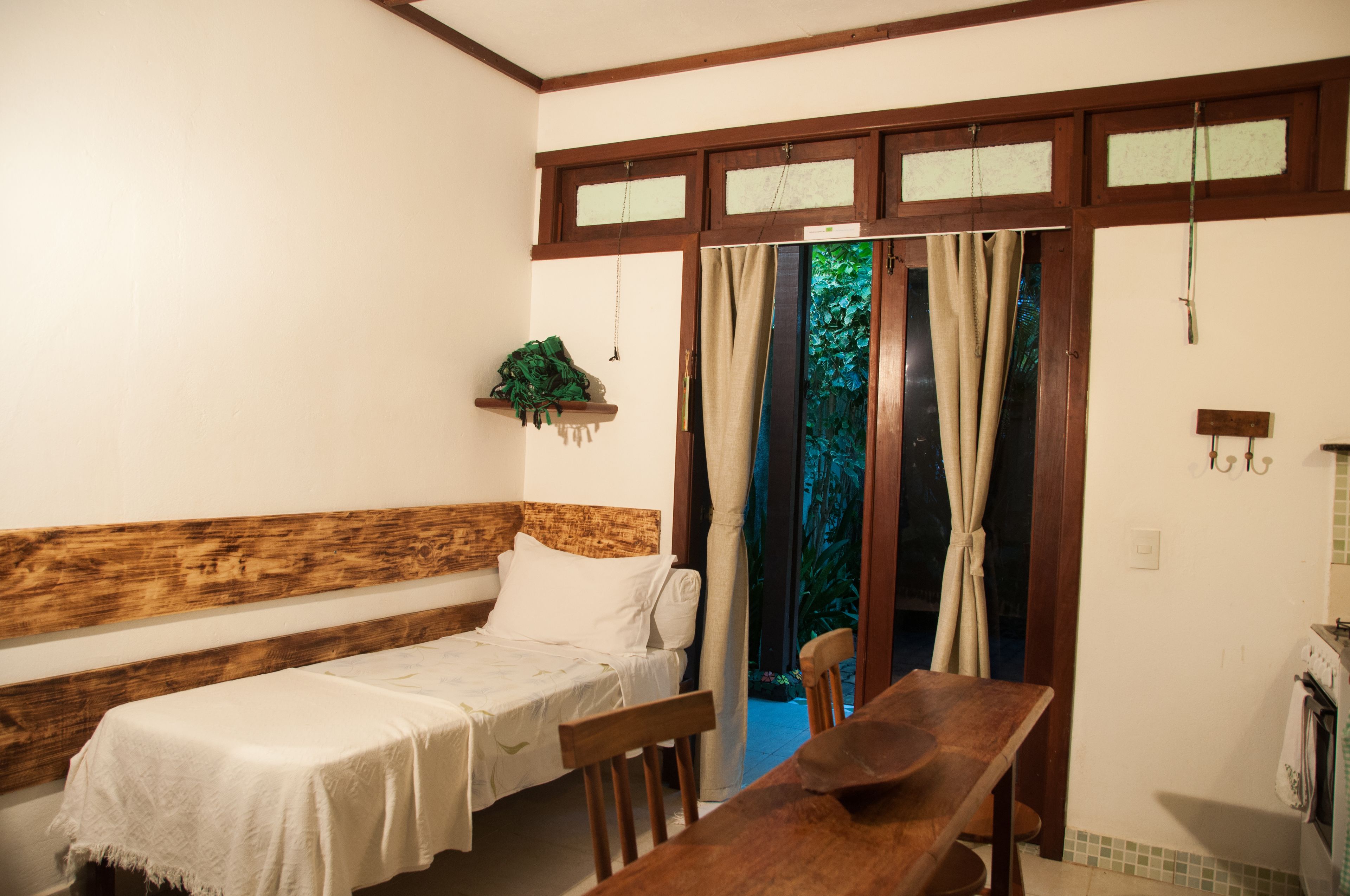Una habitación pequeña y acogedora con una cama individual, un banco de madera, una mesita y una zona de cocina.