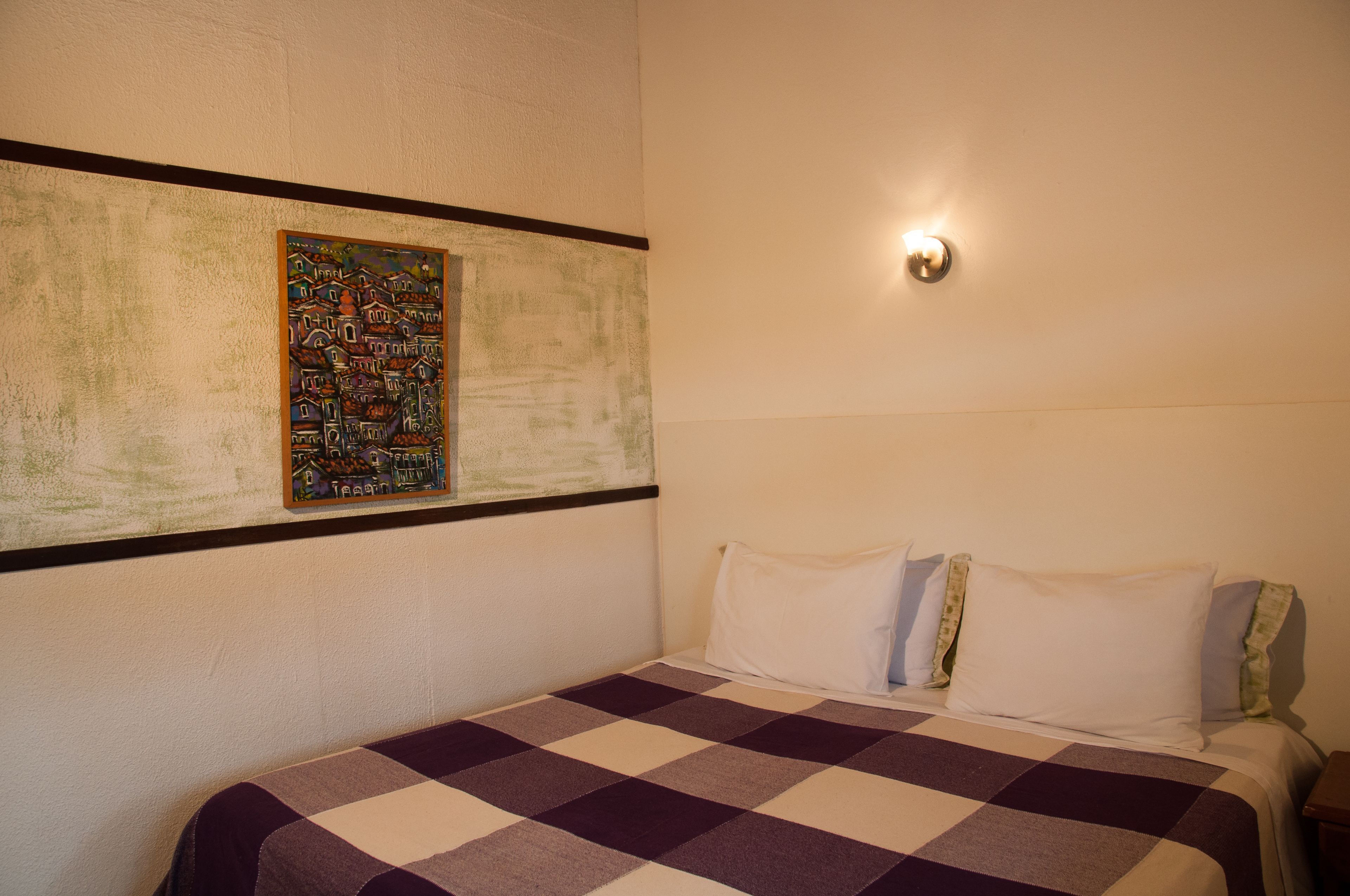 Een hotelkamer met een geruite sprei, een kunstwerk aan de muur en een bedlampje.