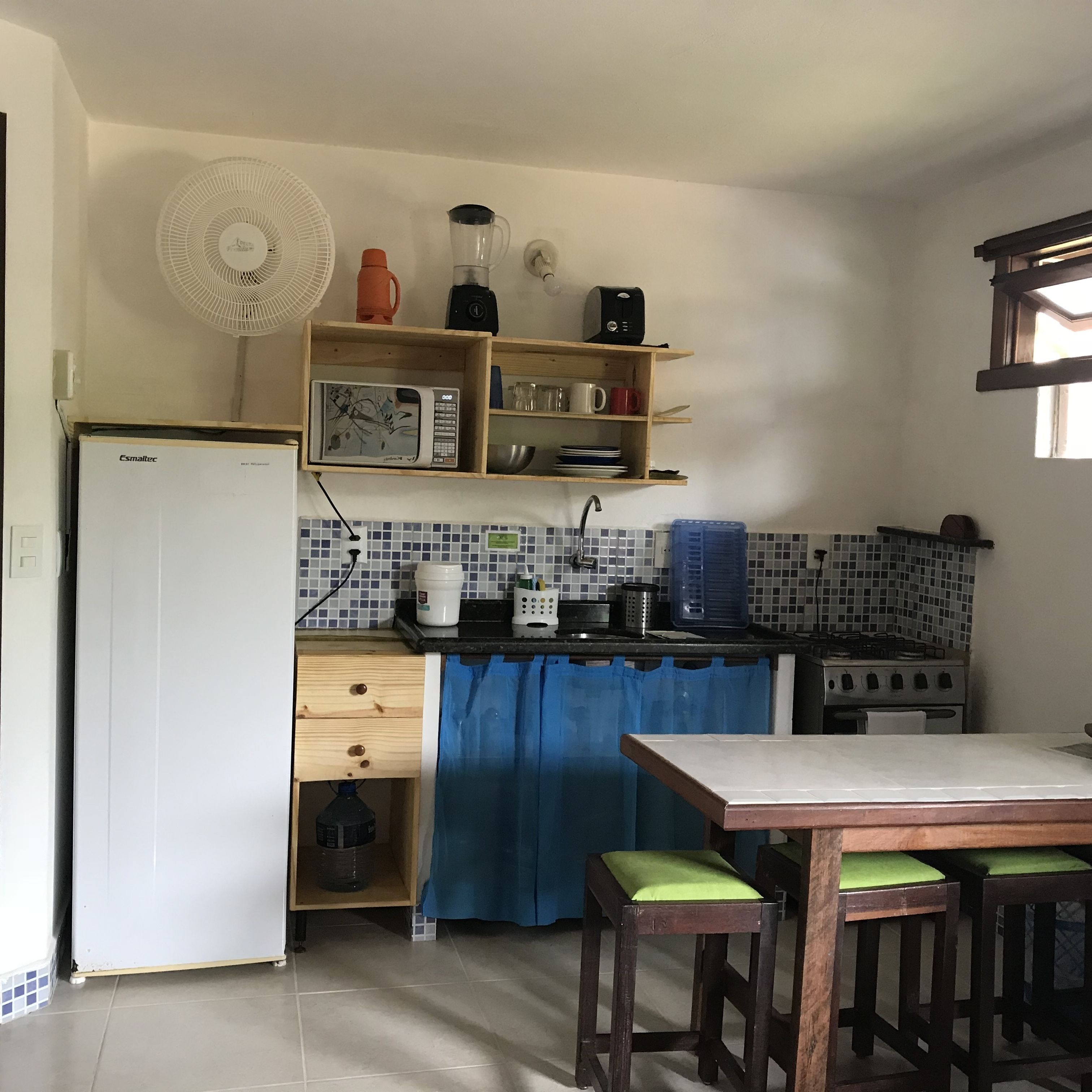 A compact kitchen with a refrigerator, microwave, stove, and a blue curtain.