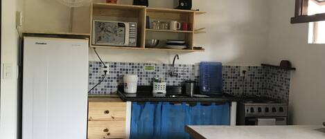 A compact kitchen with a refrigerator, microwave, stove, and a blue curtain.