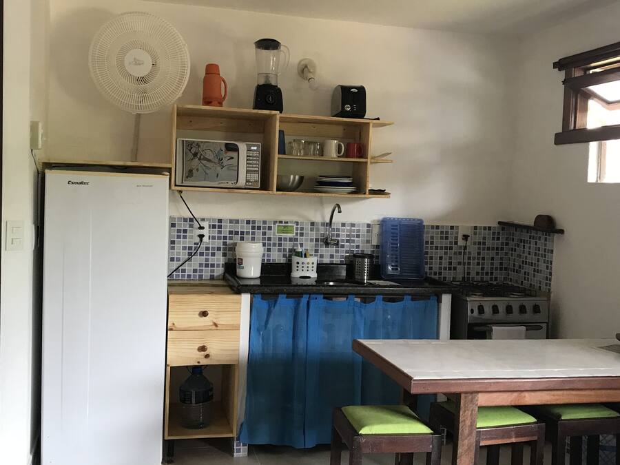 Una cocina compacta con refrigerador, microondas, estufa y una cortina azul.