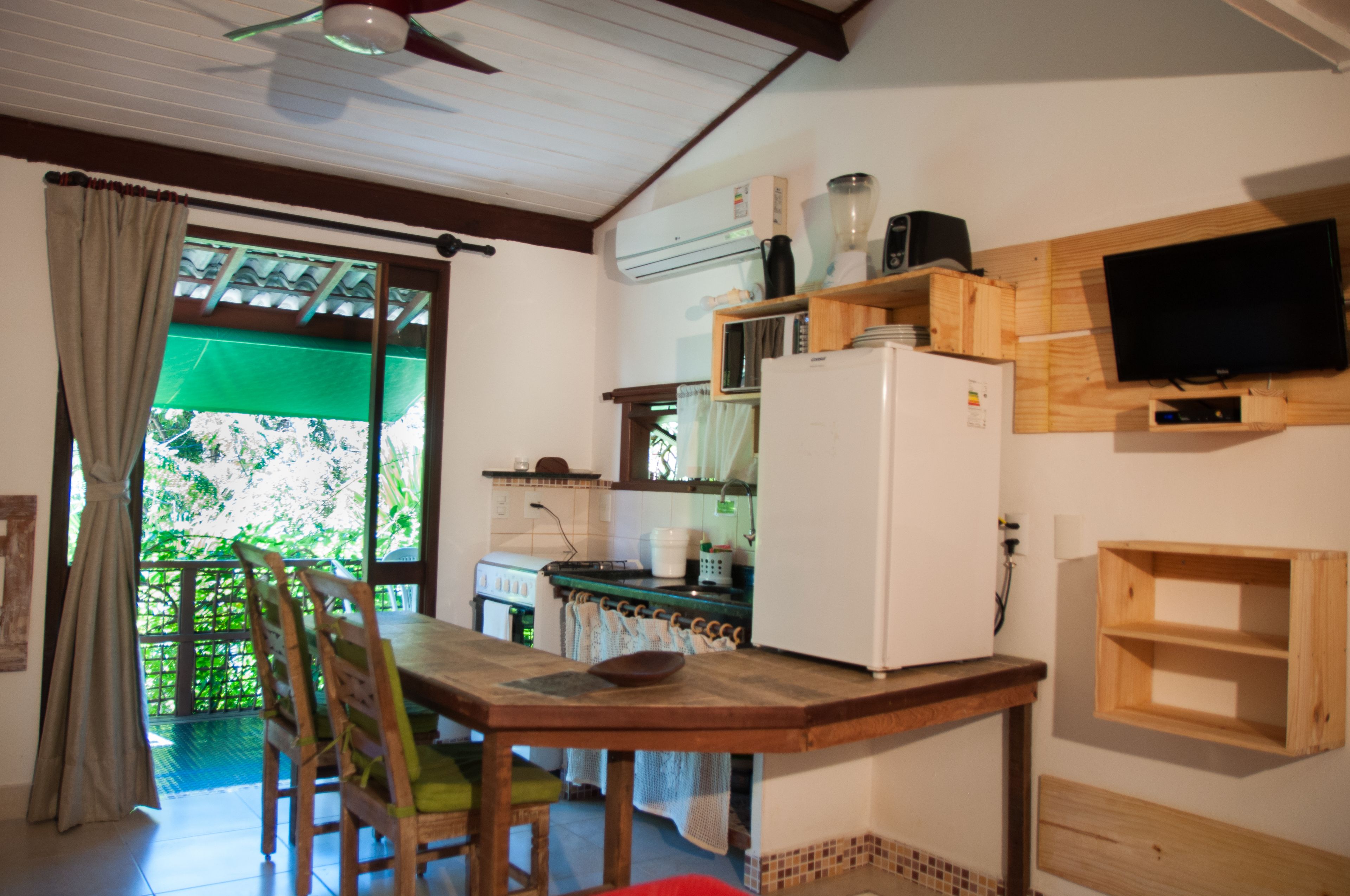 A kitchen with a dining table, chairs, a refrigerator, a microwave, a stove, and a television mounted on the wall.