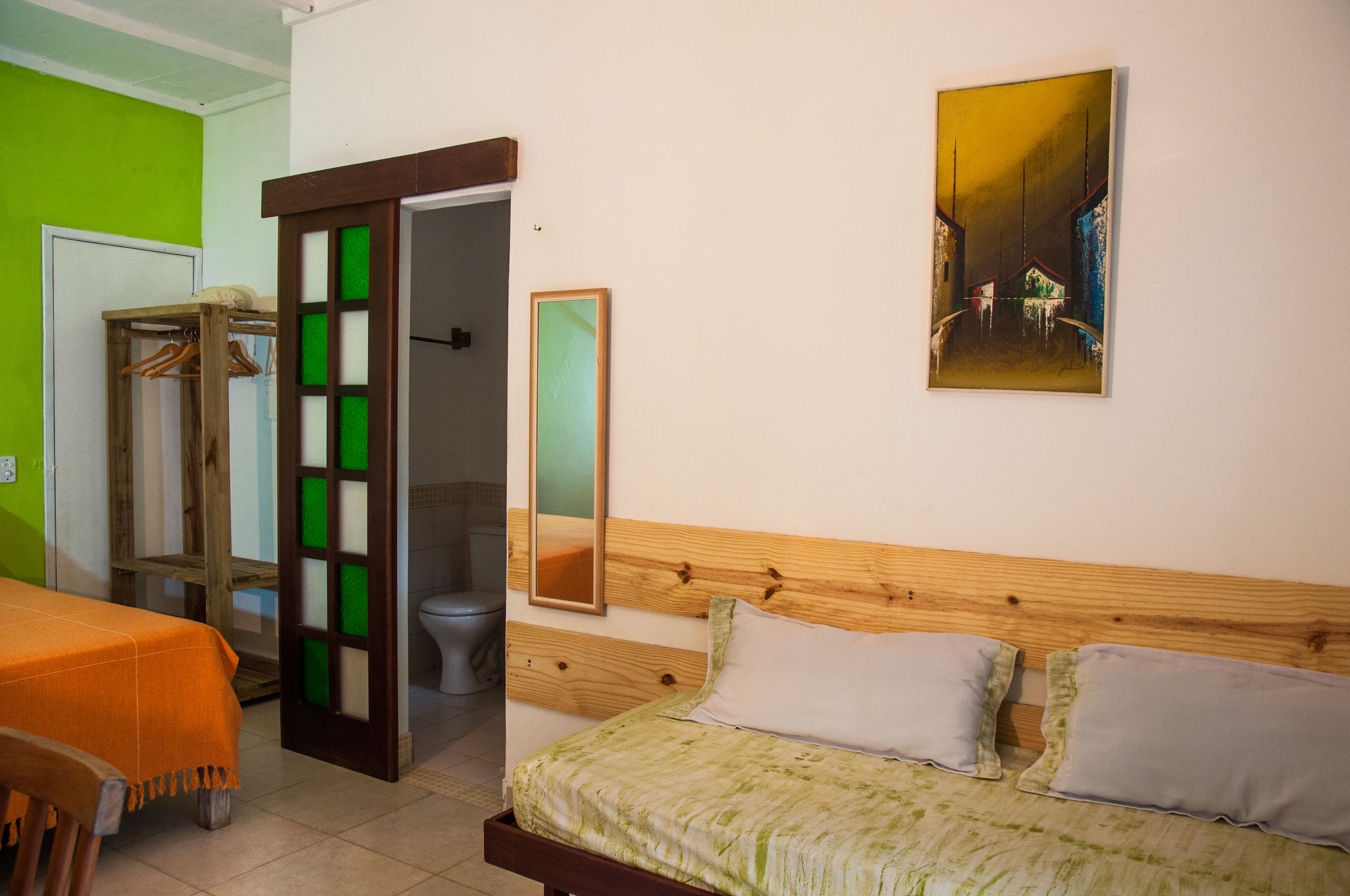 A room with a bed, a wooden headboard, a mirror, and a painting on the wall.
