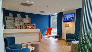 A modern bar area with seating, a television, and a variety of beverages. - Hôtel Akena Besançon (Chemaudin)