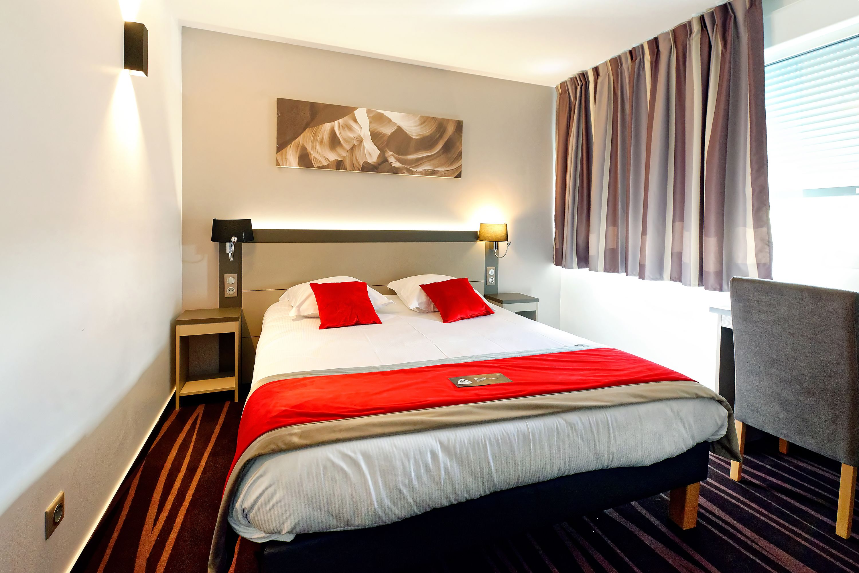 A hotel room with a neatly made bed, a bedside lamp, a small table, and a chair.