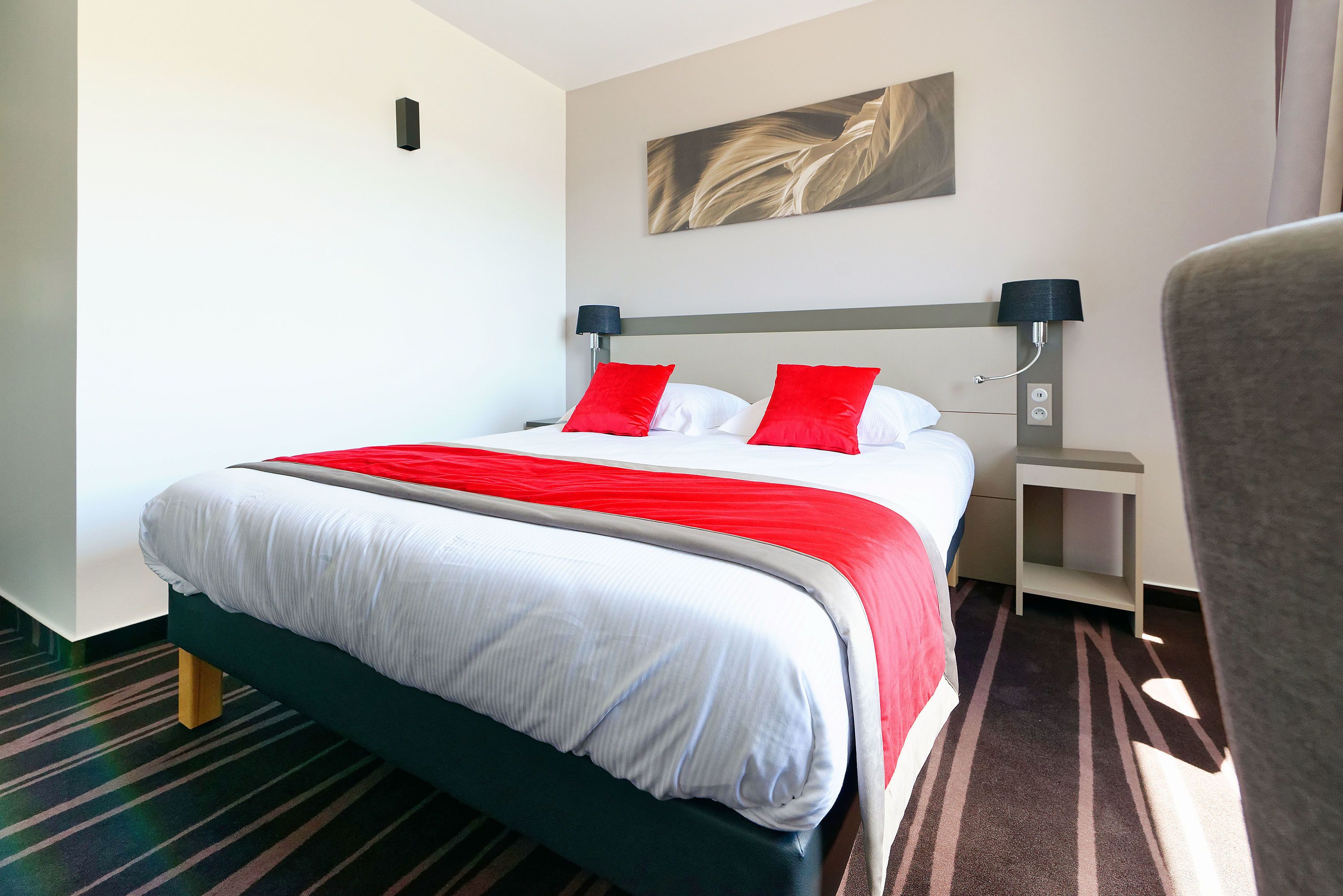 A hotel room with a bed, a nightstand, a lamp, and a chair.