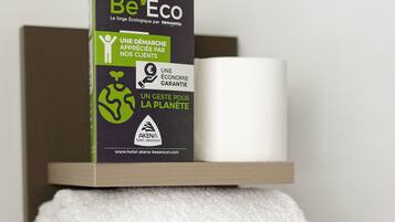 Una estantería con una caja etiquetada "Be Eco", una toalla blanca y un objeto cilíndrico blanco.