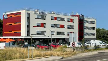 Un hotel llamado "AKENA" con un diseño moderno, que cuenta con varios pisos y un estacionamiento con varios autos.